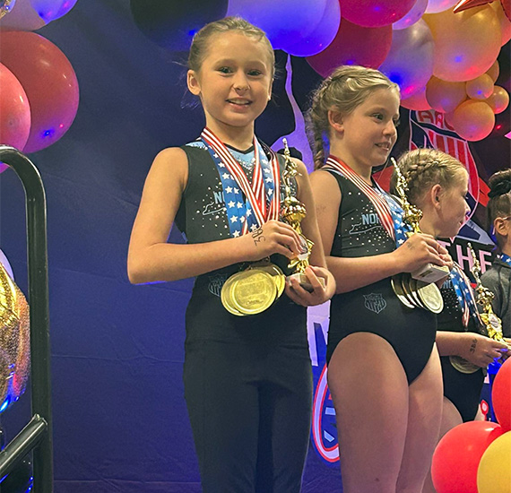 Young gymnast on the podium proudly displays her medals and trophy at a gymnastics awards ceremony.