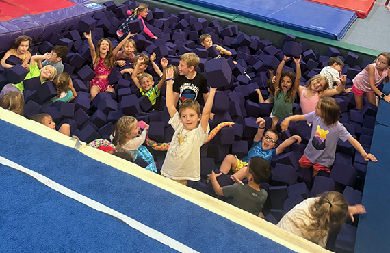 bp1 Smiling children celebrating while playing in a foam pit at CGA’s active and fun gymnastics camp.