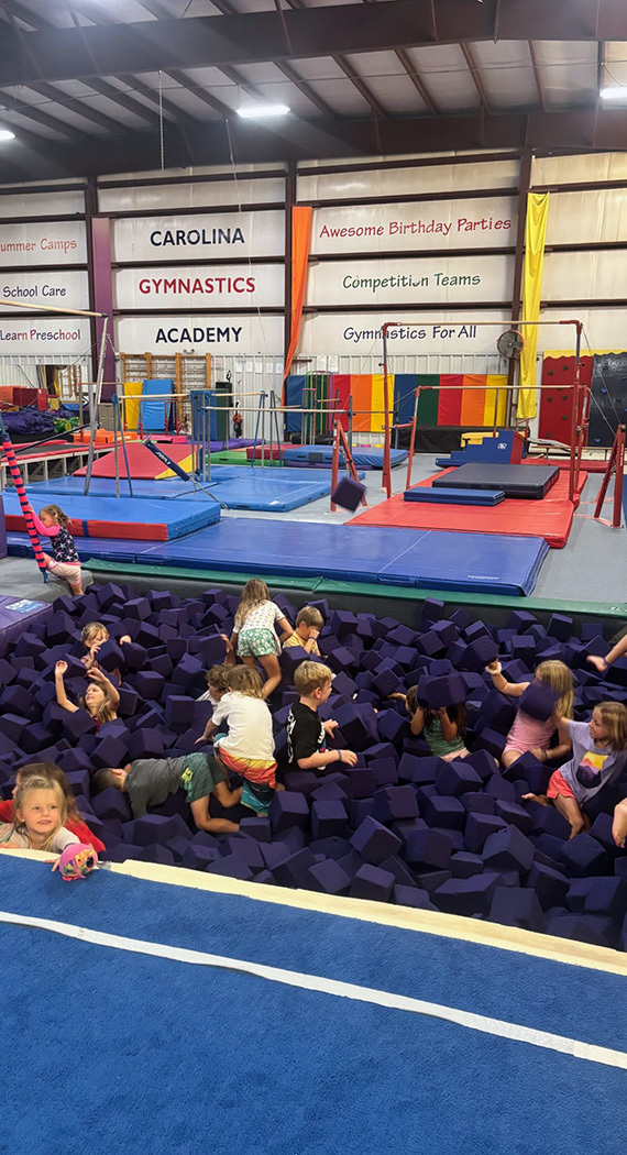 bph Children laugh and play in a giant foam pit in the gymnastics gym at Carolina Gymnastics Academy.