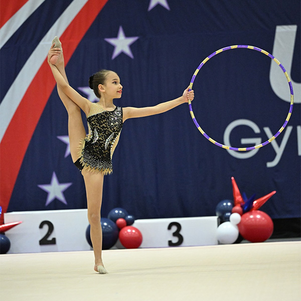 faqs Rhythmic gymnast performing a split hold while spinning a hoop in a competitive CGA event