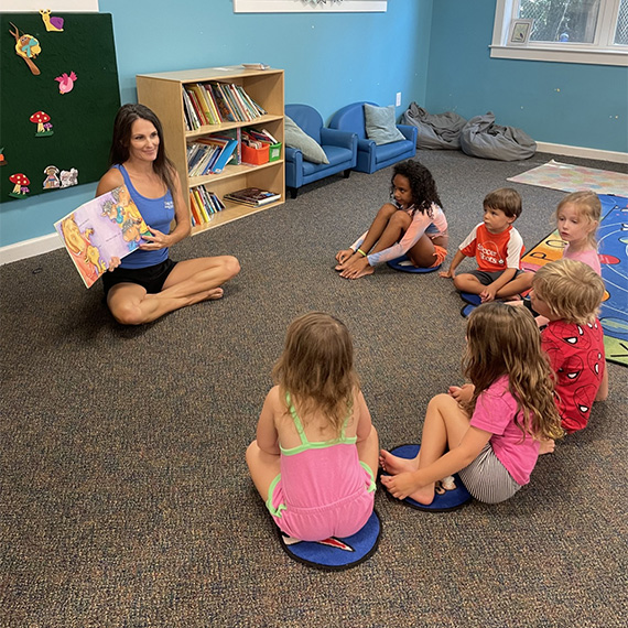 Group of young children listening to a story read aloud by their teacher at CGA’s Preschool program.