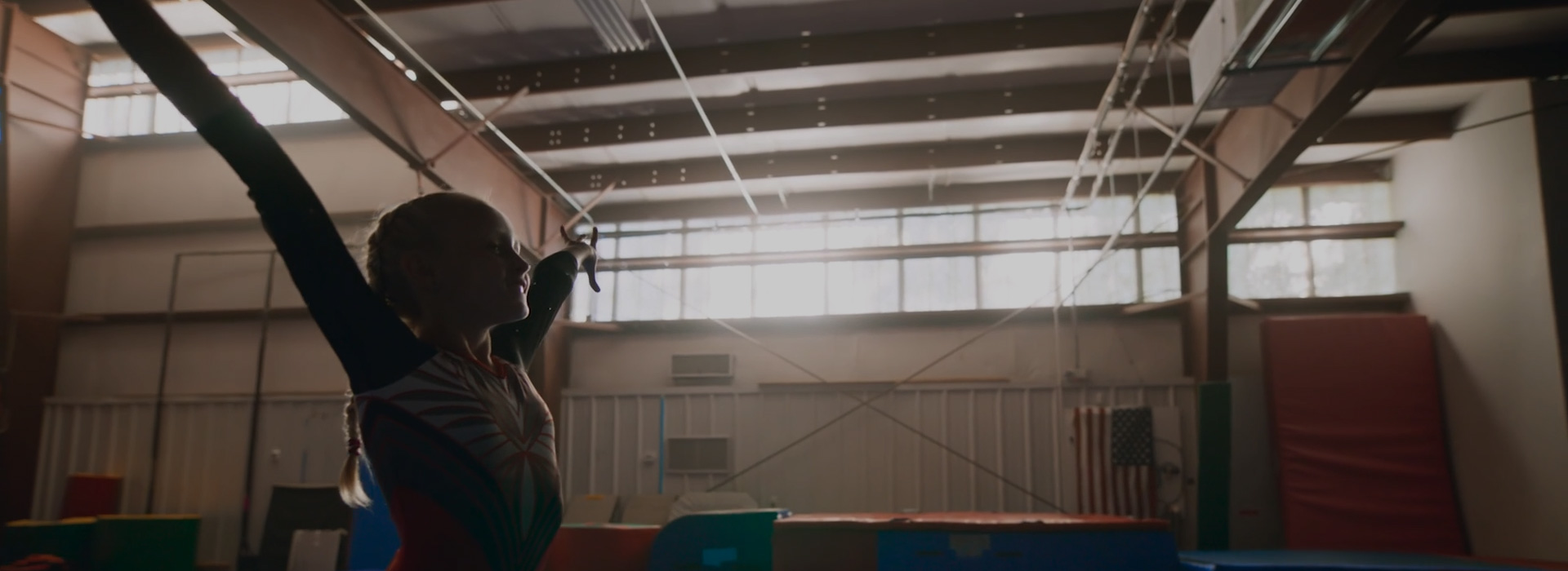 Young gymnast in leotard strikes a confident pose under natural light in indoor gymnastics facility