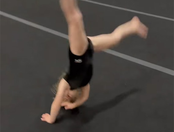 st Preschool gymnast mid-cartwheel during skills practice on the black tumbling mat at Carolina Gymnastics Academy.